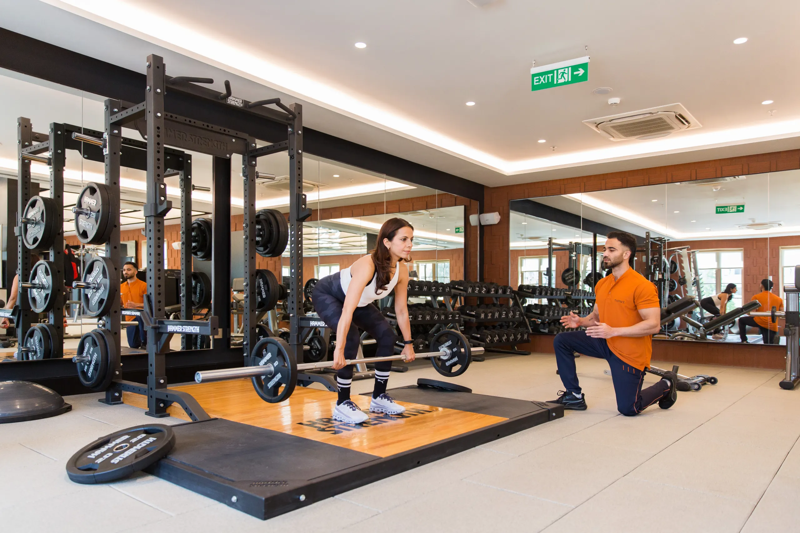 Coach supporting barbell strength training at DLF THRIVE Club 4